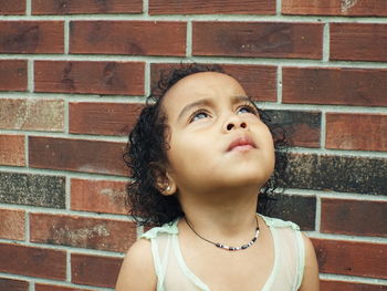 Close-up of thoughtful girl looking up while standing by brick wall