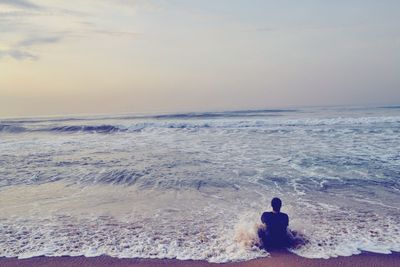 Rear view of woman sitting on beach against clear sky