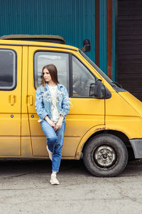 Woman  in jeans near a yellow car, van. full-length portrait of one person. holds in hands flower