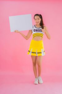 Full length portrait of woman standing against pink background