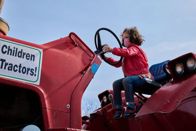 Girl in a mask pretending to drive a tractor at the county fair exhibit