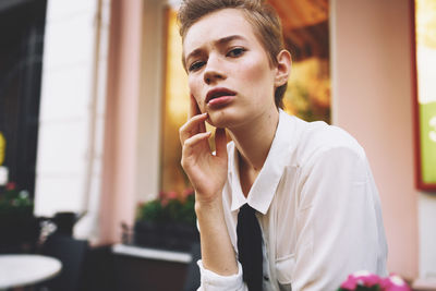 Portrait of young man looking away while sitting on window