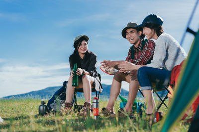 Happy friends sitting on chairs against sky