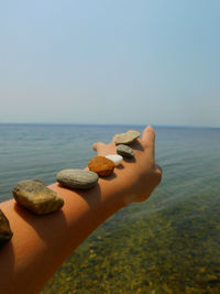 Cropped image of woman with pebbles on hand against sea