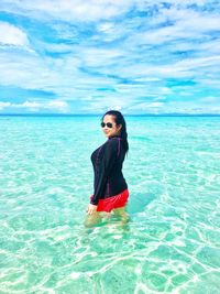 Young woman standing at beach against sky