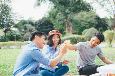 Friends toasting drinks while sitting at park