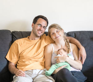 Happy mother and father holding baby at sofa at home