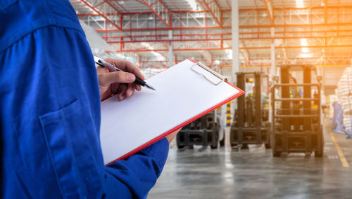 Midsection of male supervisor writing on paper at factory