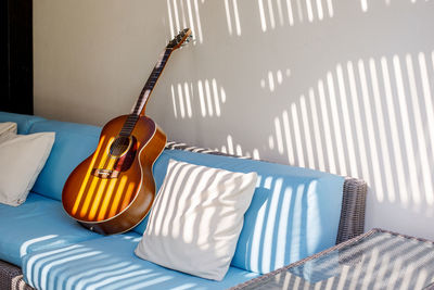 An acoustic guitar stands on a blue sofa next to a pillow on the terrace