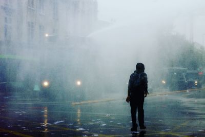 Rear view of man walking on street during rainy season