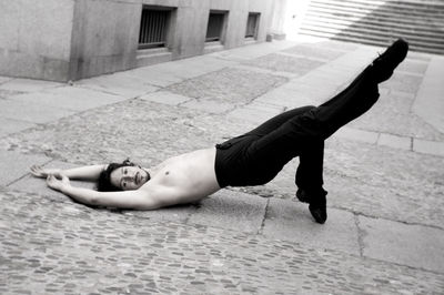 Portrait of shirtless man lying on footpath