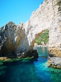Rock formations by sea against clear blue sky