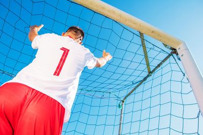 Low angle view of man standing by net against sky