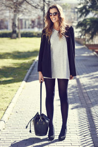 Happy young woman holding handbag while standing on footpath