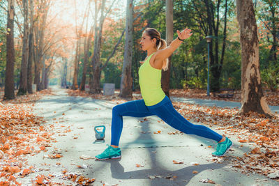 Full length of woman with arms raised on autumn leaves