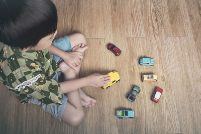 High angle view of boy playing with toy cars on hardwood floor 