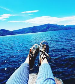 Low section of woman relaxing on sea against sky