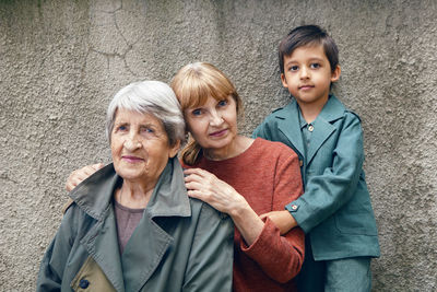 Three generations grandmother great grandmother grandson are standing on the street against a gray 