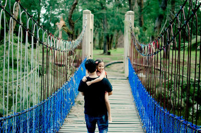 Rear view of father carrying daughter while walking on footbridge in park