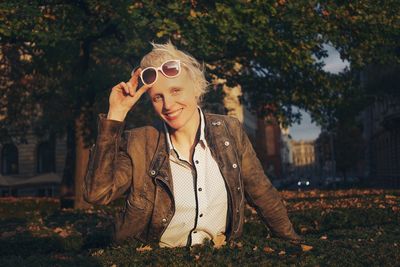 Portrait of mid adult woman holding sunglasses while standing against trees