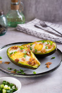 Baked avocado with egg, bacon and chives on a plate on the table for a keto diet vertical view