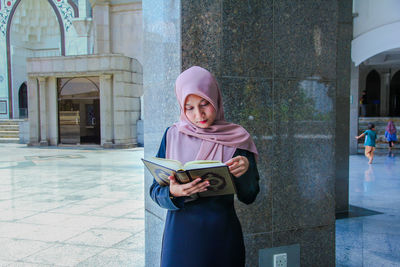 Woman reading koran against building