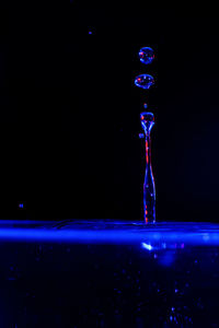 Close-up of drop falling on glass against black background