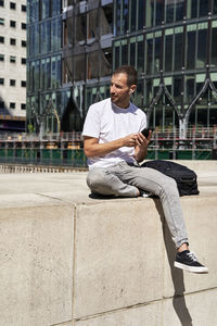 Man with smart phone sitting in front of building