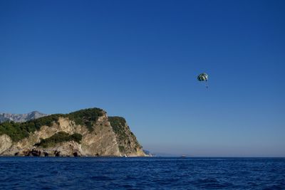 Person parasailing over sea against clear blue sky