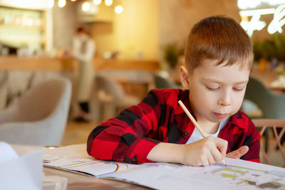 Handsome little boy draws at the table with a pencil. waiting for an order in a cafe. the boy draws 