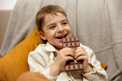 Little adorable boy sitting on the couch at home and eating chocolate bar. child and sweets