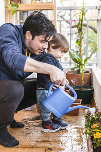 Man and boy watering plant together while standing at balcony