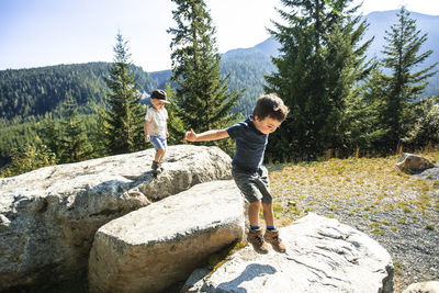 Young boys jumping, exploring on rocks in natural setting.