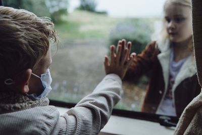 Boy touching glass while looking at girl standing outdoors