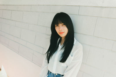 Portrait of young woman standing against wall