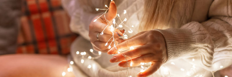 Woman in a cozy comfy knitted wool white sweater holding in hands and untangle glowing lights