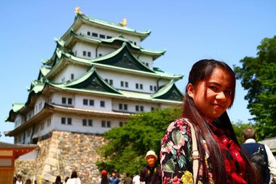 Portrait of smiling woman standing against building in city during sunny day