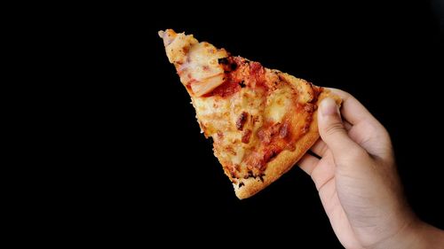 Close-up of hand holding pizza over black background