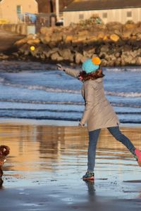 Young woman throwing ball for dog on a beach during winter