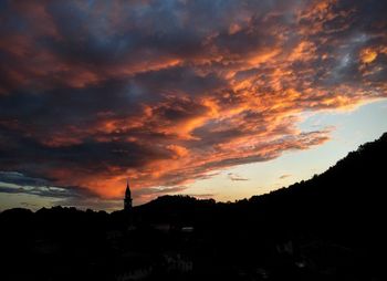 Silhouette trees and buildings against dramatic sky during sunset