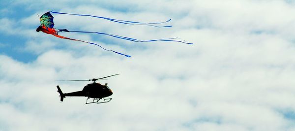 Low angle view of helicopter and kite flying against cloudy sky