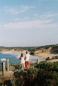 Friends standing on shore against sky