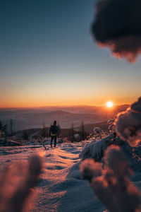 People on snowy field against sky during sunset