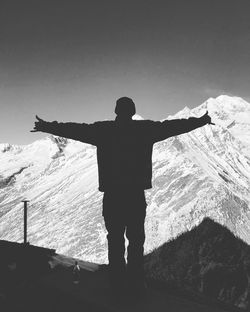 Silhouette man with arms outstretched standing against snow capped mountains