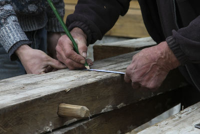 Midsection of carpenters measuring wood while working in carpentry workshop