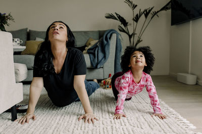 Mother and daughter practicing yoga in living room at home