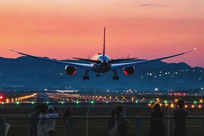 Airplane flying over airport runway against sky during sunset