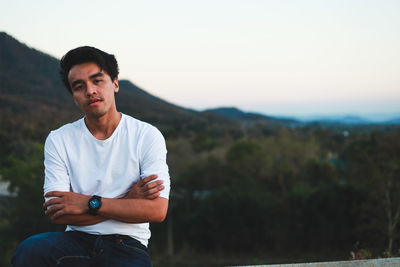 Portrait of young man sitting against mountains