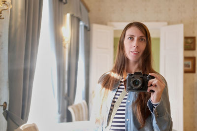 A girl with long hair, in jeans, takes a selfie on the camera, in the mirror