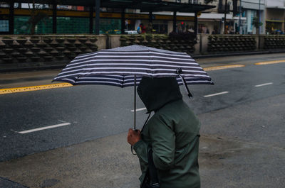 Rear view of man with umbrella walking on road